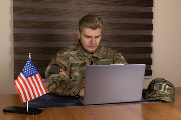 Man in military uniform using laptop in desert outpost