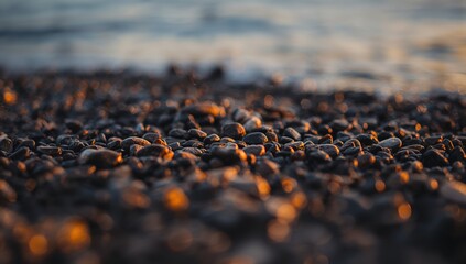 Obraz premium Close-up of smooth black and orange pebbles on the beach with a soft sunset glow, natural texture for banner background.