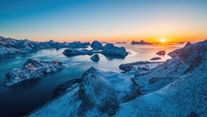Aerial view of a winter sunset over the sea with snow-covered islands, mountains, and a winding road, showcasing seasonal change