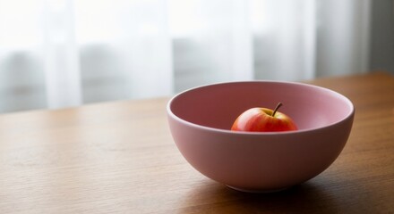 A red apple in a pink bowl on a wooden table – simplicity as luxury, an apple as a symbol, minimalist poetry, morning light.