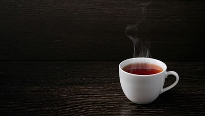 Cup of hot tea with steam on a dark rustic surface, beneficial warm beverage choice