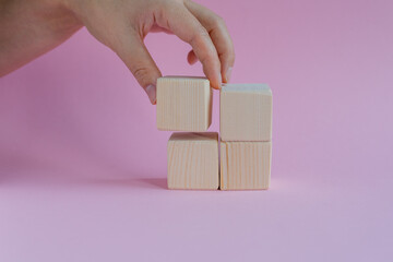 The last piece of a wooden cube in hand, assembling wooden puzzles, stacking them on a pink...