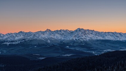 Expansive panoramic scene of snow-capped mountain peaks glowing under a warm evening sky in a western mountain range.