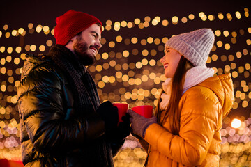 Funny festive moment a couple share hot drinks under twinkling lights in a winter city Christmas market