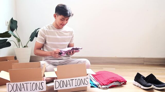 Young asian volunteer happily sorting clothes for donation at home