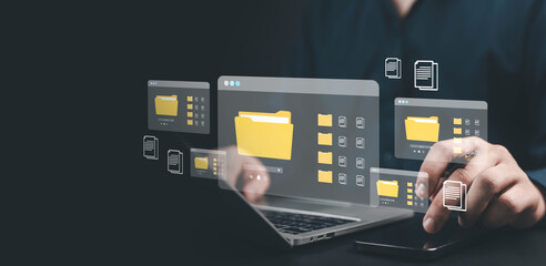 Businessman using laptop and smartphone with digital folder icons, symbolizing cloud storage, data management, modern document organization technology folder with digital documents floating around.