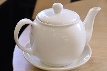 A white tea pot sits on a decorative saucer, perfect for serving hot beverages