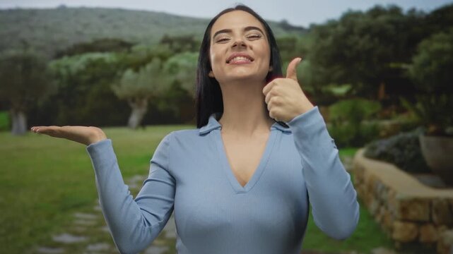 Young hispanic woman in park gestures with thumb up and smiles creating a positive outdoor vibe against a lush green backdrop