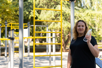 A plus-size woman wearing a black leggins and a black T-shirt is jumping rope or drinking water...