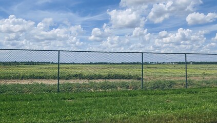 Fototapeta premium A large construction area for suburban housing is concealed by mesh and plastic barriers within a chain-link enclosure, transforming former ranchland in a southern region.