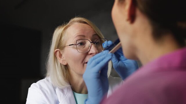 Female therapist examining patient's throat using medical spatula and flashlight