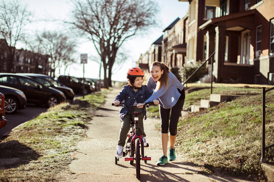 Young mother helping son ride bike in neighborhood