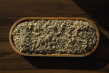 Wooden bowl with sunflower seeds on dark background