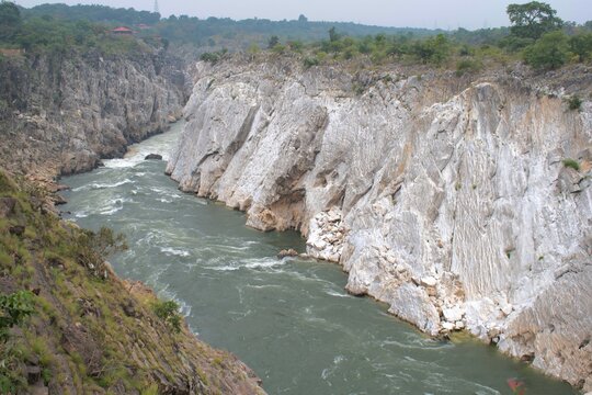 magnificent view of the narmada river carving through towering white marble cliffs at bhedaghat, creating a dramatic natural canyon surrounded by lush greenery
