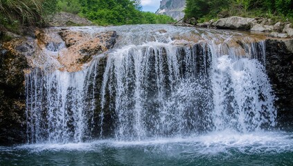 Fototapeta premium Alpine waterfall cascading down rocky terrain, summer backdrop, erosion risk