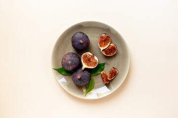 Purple ripe figs and slices with leaves on a plate top view on a stone background