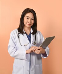 Portrait of asian female doctor in medical uniform with stethoscope on peach color background.

