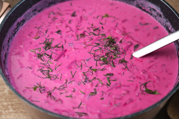 Lithuanian cold beet soup (šaltibarščiai) in a pot with a ladle. Captured in a close-up shot. Made from fresh red beets, cucumber, and kefir, sprinkled with chopped dill.