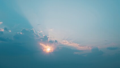 Sun setting behind clouds under a bright blue sky