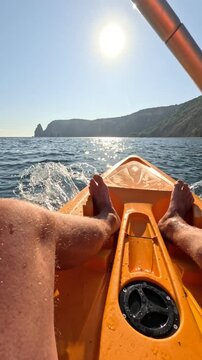 Kayaking paddling ocean, person on yellow kayak in sunny sea, mountains in background. Vertical video.