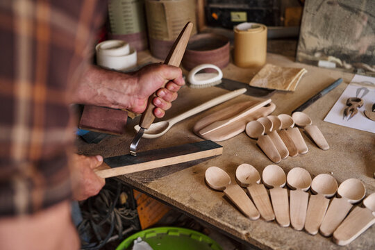 Craftsman sharpening carving tool, wooden spoons in workshop, handmade craft, artisan woodworker, traditional carving, woodworking process, hobby and creative occupation, craftsmanship