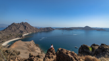 A man enjoys a view on majestic mountains of Padar Island, alongside calm waters dotted with charming boats, creating an idyllic and serene coastal landscape that delights, Komodo, Indonesia