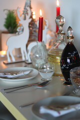 Table set for Christmas meal, with plates, wine, decorations and lit candles. Selective focus.