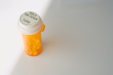 A focused view of an orange prescription medicine bottle lying down with yellow pills inside, casting a distinct shadow on a bright white surface.