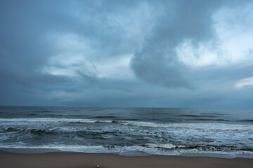 Overcast sea view. Dark waves under a cloudy blue-grey sky create a moody seascape. The horizon fades softly into the mist.