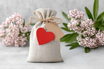 Elegant linen pouch with heart tag and ribbon for branding or gift packaging on neutral background featuring floral accents