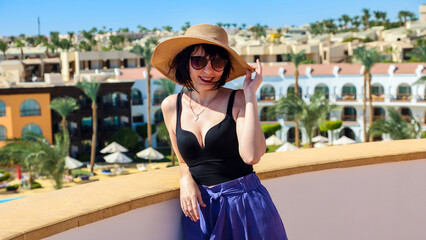 Fototapeta premium A girl a hat and glasses on a terrace with a gorgeous view of the sea, mountains and palm trees.