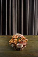 assorted meats on a wooden base with sauces and tomatoes