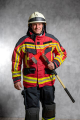 Feuerwehrmann in Einsatzuniform mit Feuerwehraxt, Studioaufnahme vor Betonwand.