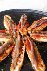 Tapas with anchovies, red pepper and bread on a black plate