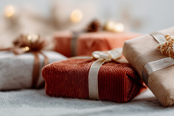 A collection of beautifully wrapped Christmas gifts in various colors, including red, gold, and silver, arranged on a soft surface with warm bokeh lights in the background.