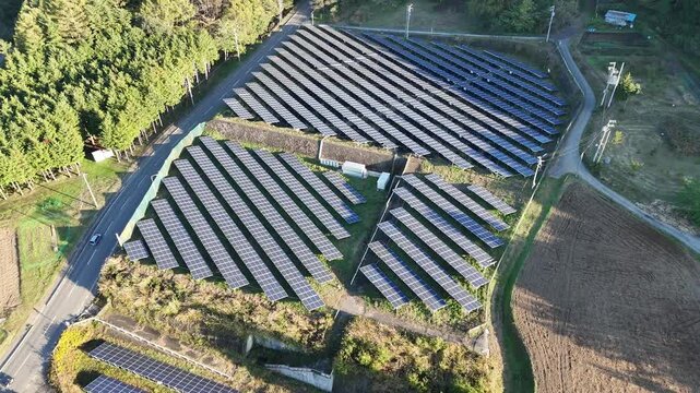A large field with solar panels and a white building in the middle. The solar panels are arranged in rows and the field is surrounded by a fence