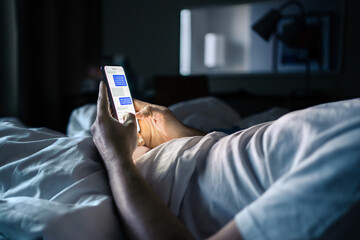 Phone in bed. Text message. Man texting. Screen time at night. Using smartphone messenger app in...