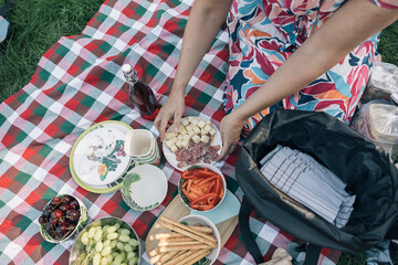 Unrecognizable person arranging food on a picnic blanket, including cheese, salami, grapes, cherries and breadsticks