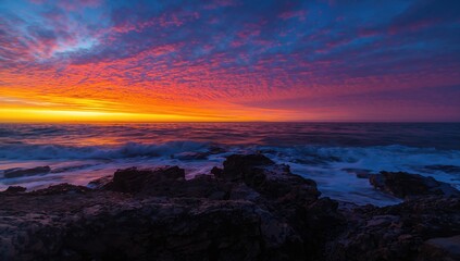Fototapeta premium Dramatic sunrise over a rugged shoreline with vibrant hues of orange and blue, highlighting the beauty of nature