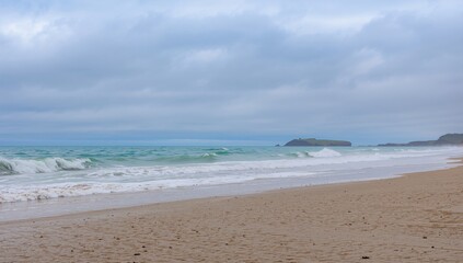 Fototapeta premium Majestic ocean waves crashing onto the beach beneath a cloudy sky, erosion risk