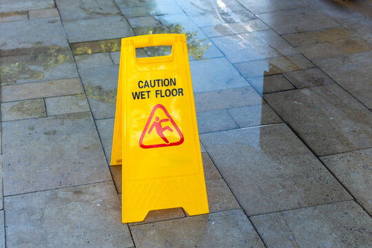 Caution wet floor sign on wet stone floor - Powered by Adobe