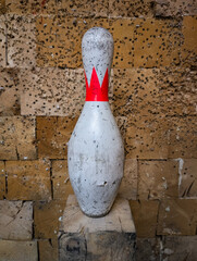 Vintage white bowling pin with red crown used as a makeshift target, standing on wood block against...