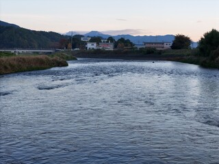 A river with a bridge in the background. The water is calm and clear. The sky is a mix of blue and orange