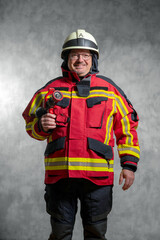 Feuerwehrmann in Einsatzuniform mit Hohlstrahlrohr für die Brandbekämpfung, Studioaufnahme vor Betonwand.