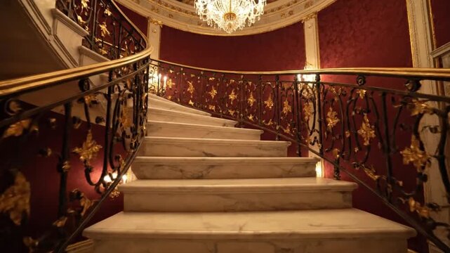 An elegant marble spiral staircase with ornate gold railings and a sparkling crystal chandelier