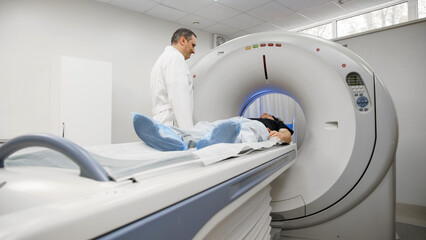 Medical professional assisting patient on CT scanner table, preparing for tomography imaging in a bright, modern diagnostic room with advanced medical technology