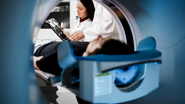 Medical professional analyzing CT scan results while patient lies on examination table inside CT scanner, showcasing advanced imaging technology and diagnostic procedures