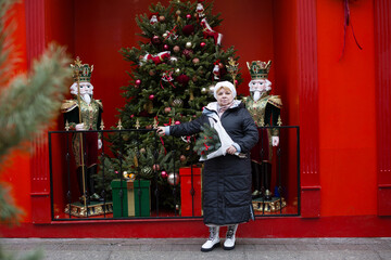 A white woman in a fur hat with long blonde hair holds a bouquet of pine branches decorated with...