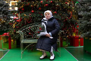 A white woman in a fur hat with long blonde hair holds a bouquet of pine branches decorated with...