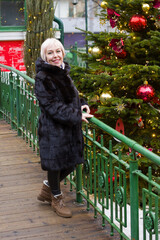 A smiling white woman with short hair stands by a decorated Christmas tree. She's wearing a black...